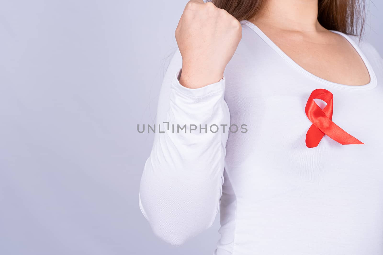 Red AIDS awareness ribbon on woman chest and raise her hand to fight them on grey background. World Aids Day, Healthcare and medical concept.