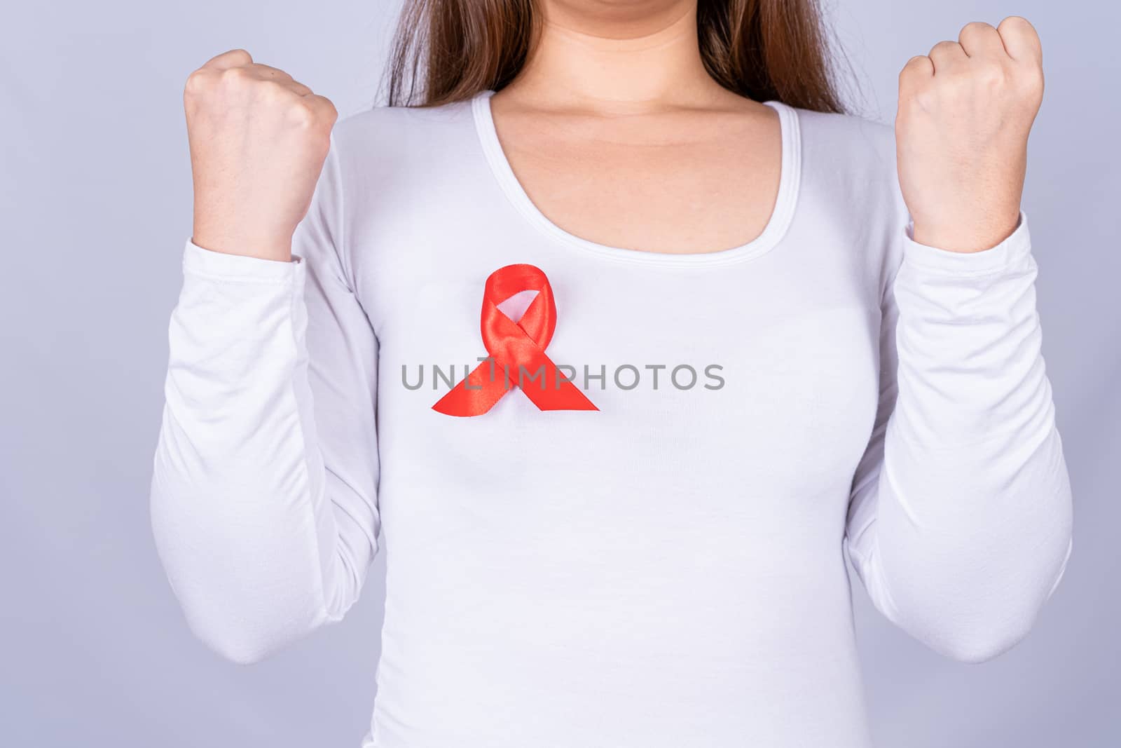 Red AIDS awareness ribbon on woman chest and raise her hand to fight them on grey background. World Aids Day, Healthcare and medical concept.