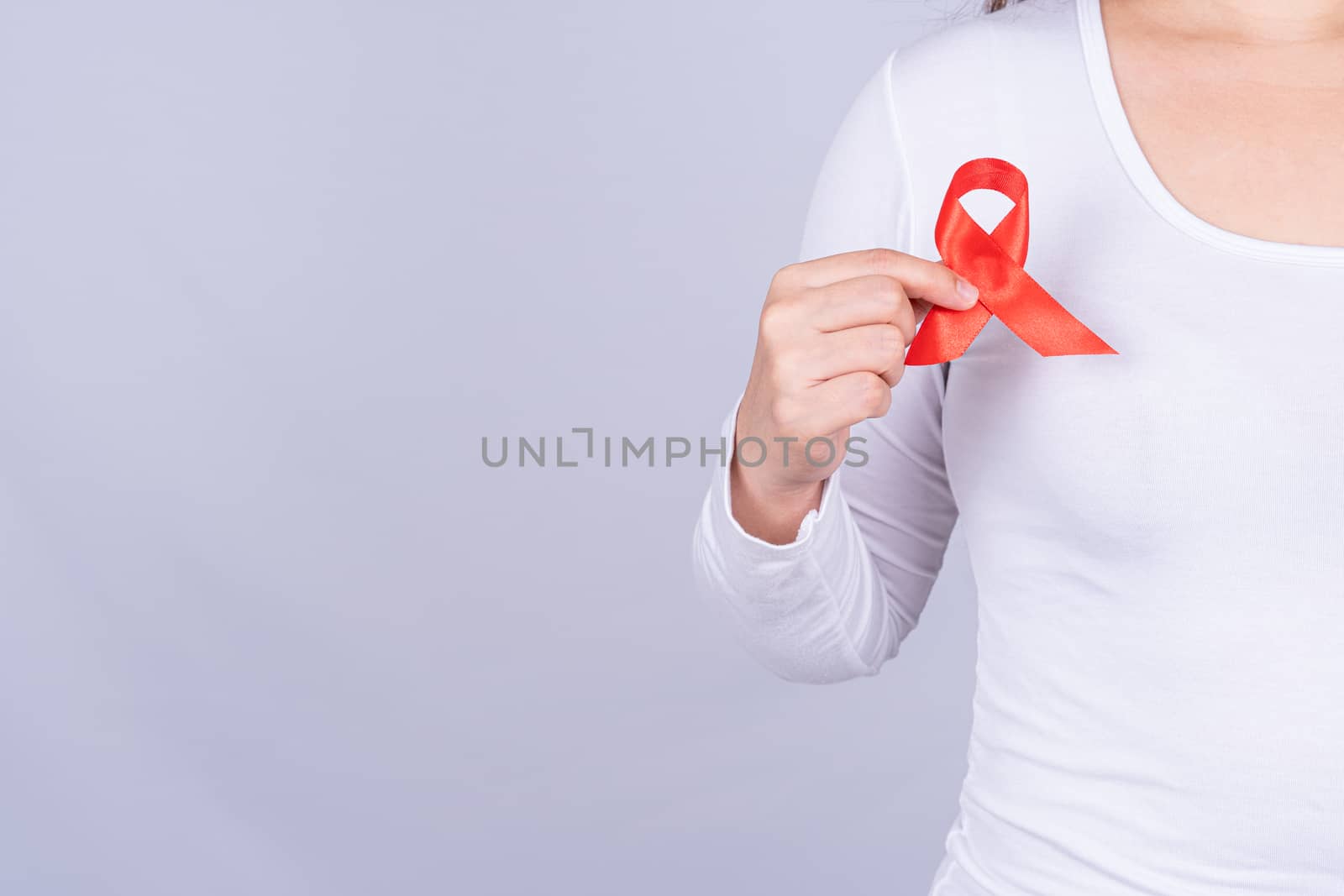 Red AIDS awareness ribbon on woman chest and raise her hand to fight them on grey background. World Aids Day, Healthcare and medical concept.