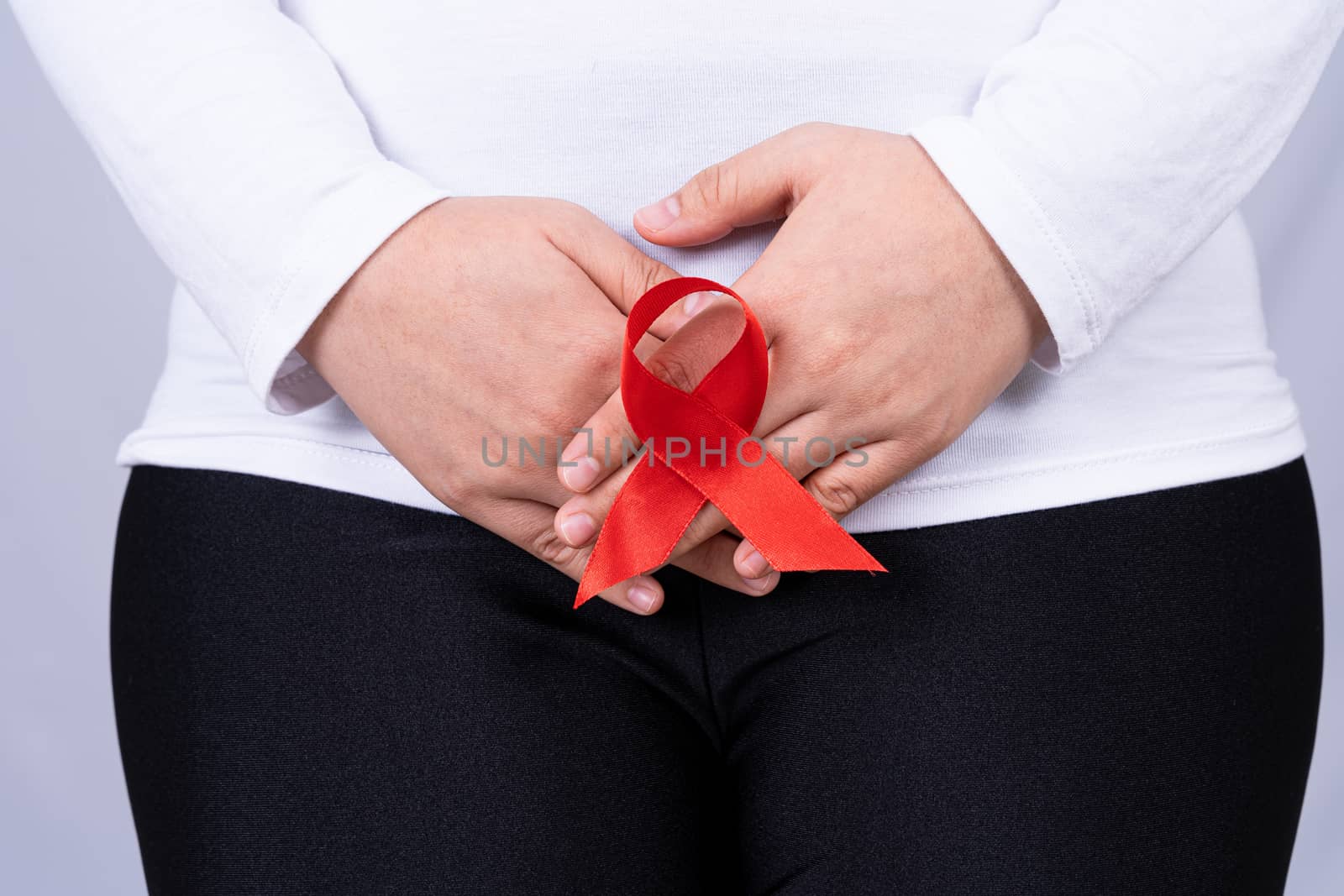 Woman hands holding her crotch with Red AIDS awareness ribbon on grey background. Medical, healthcare for advertising concept.