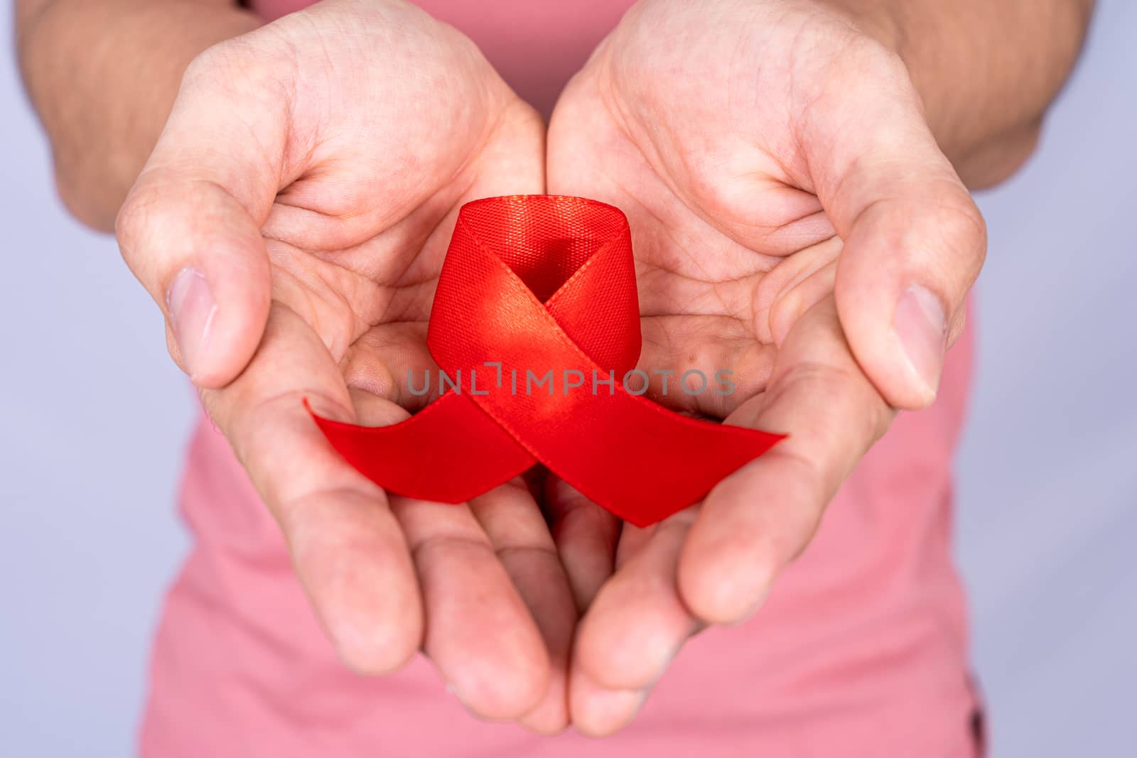 Red AIDS awareness ribbon holding by man on grey background. World Aids Day, Healthcare and medical concept.