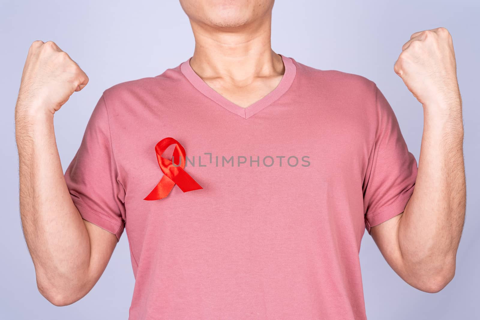 Red AIDS awareness ribbon on man chest and raise his hand to fight them on grey background. World Aids Day, Healthcare and medical concept.