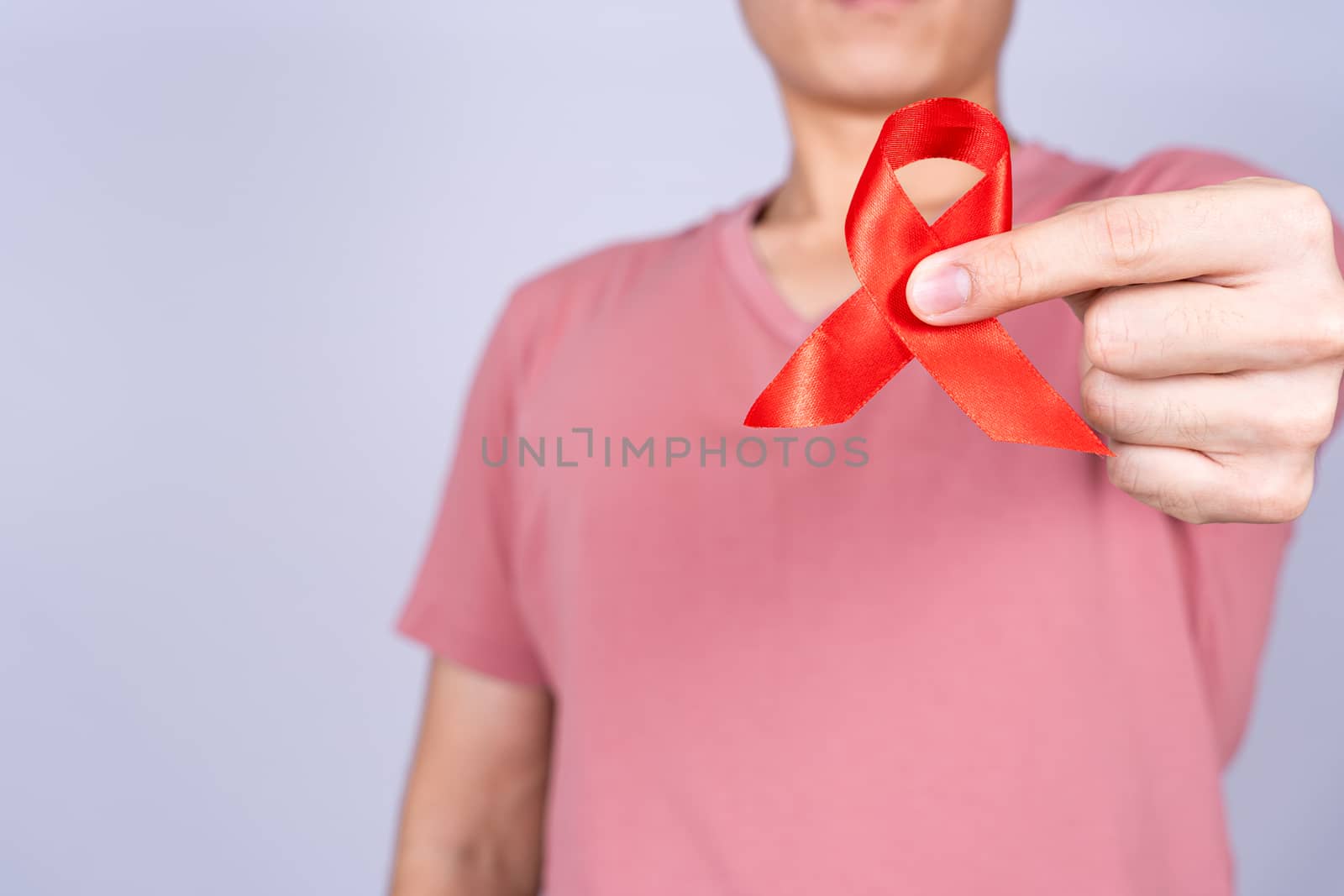 Red AIDS awareness ribbon holding by man on grey background. World Aids Day, Healthcare and medical concept.