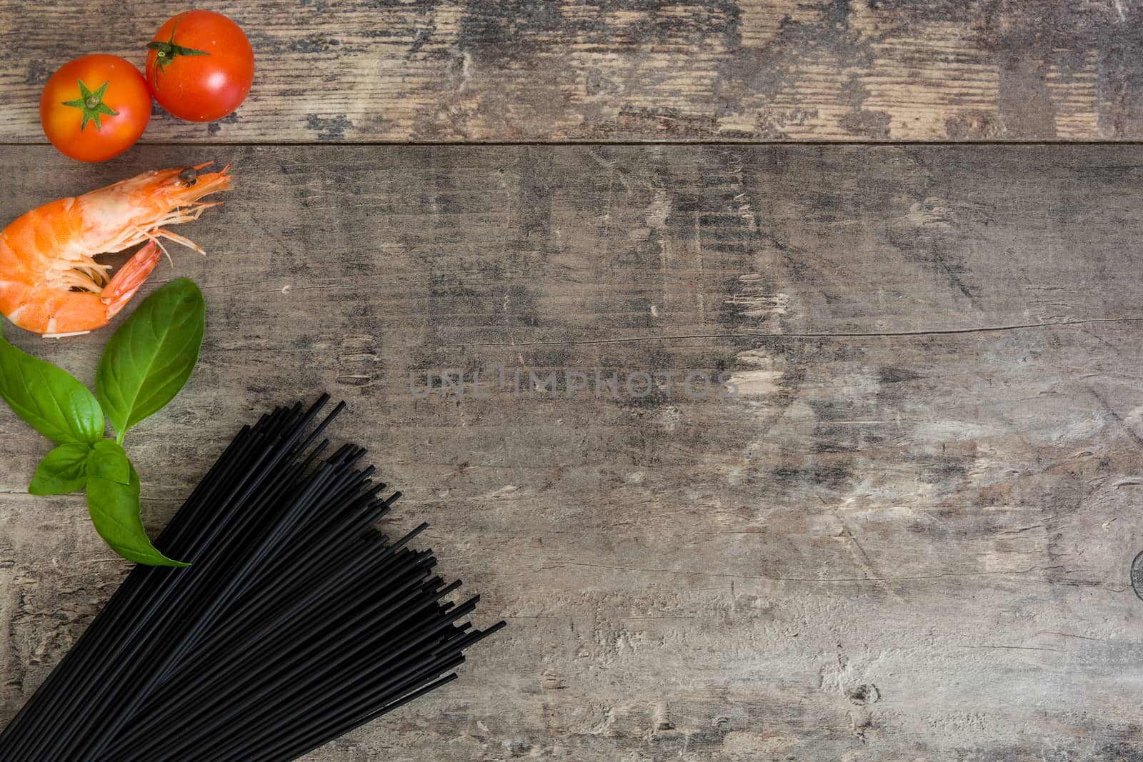 Raw black spaghetti with prawns, tomatoes and basil on wooden background