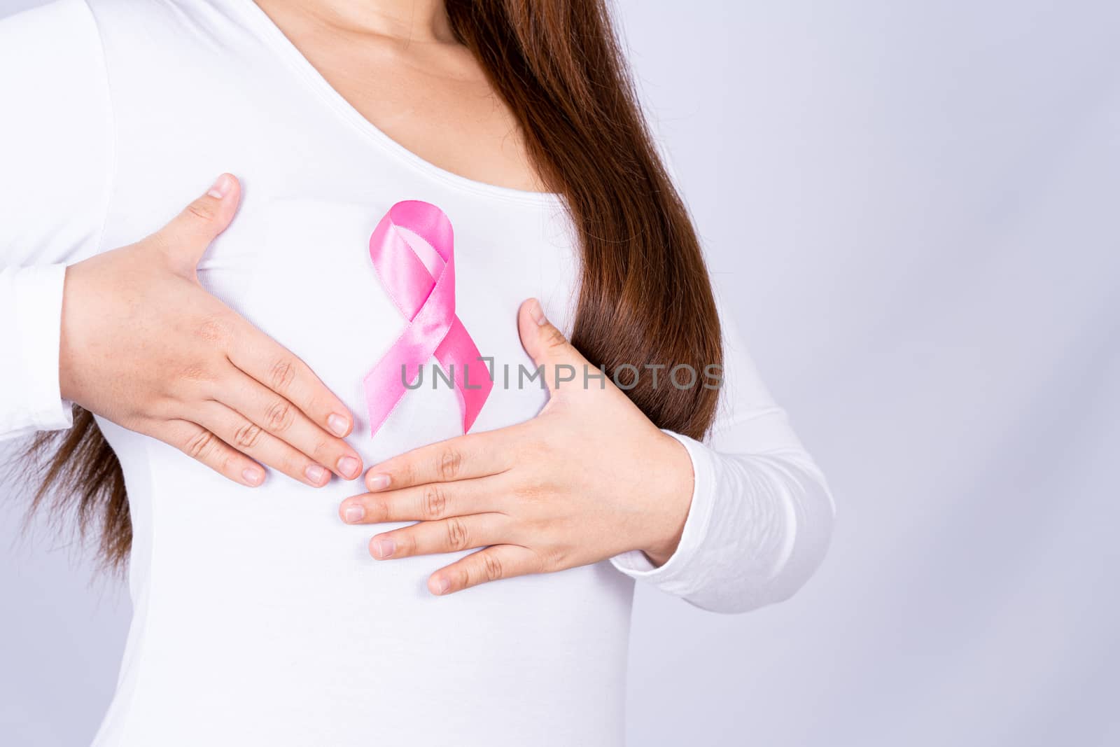Breast cancer awareness ribbon on woman chest and doing self exam on grey background. Medical, healthcare for advertising concept.