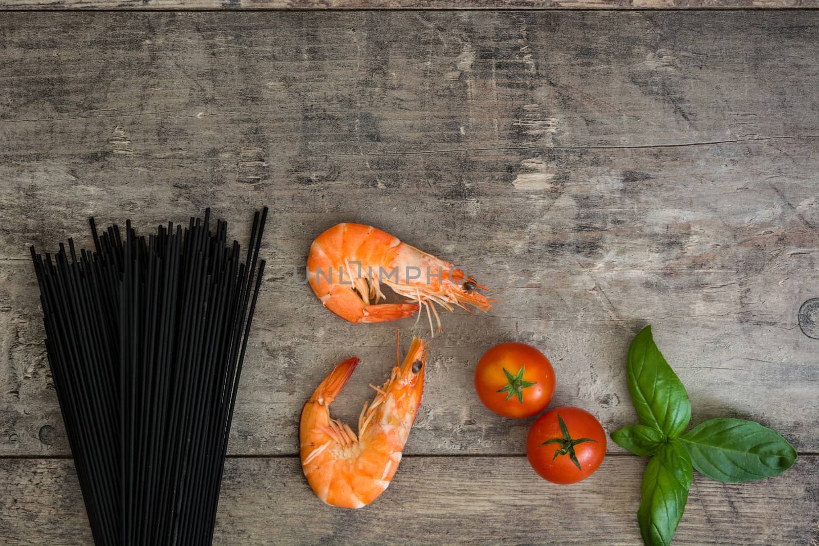 Raw black spaghetti with prawns, tomatoes and basil on wooden background by chandlervid85