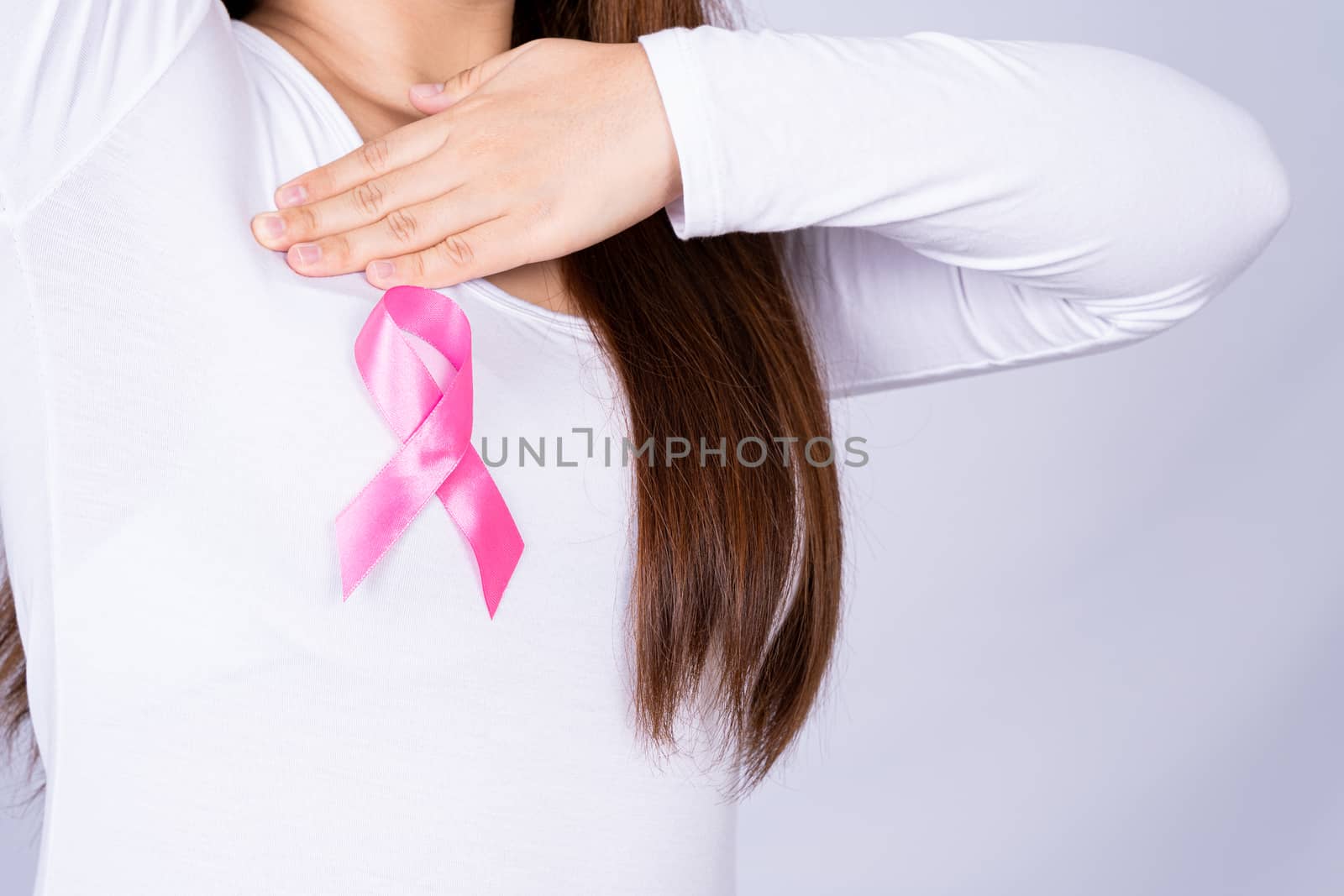 Breast cancer awareness ribbon on woman chest and doing self exam on grey background. Medical, healthcare for advertising concept.