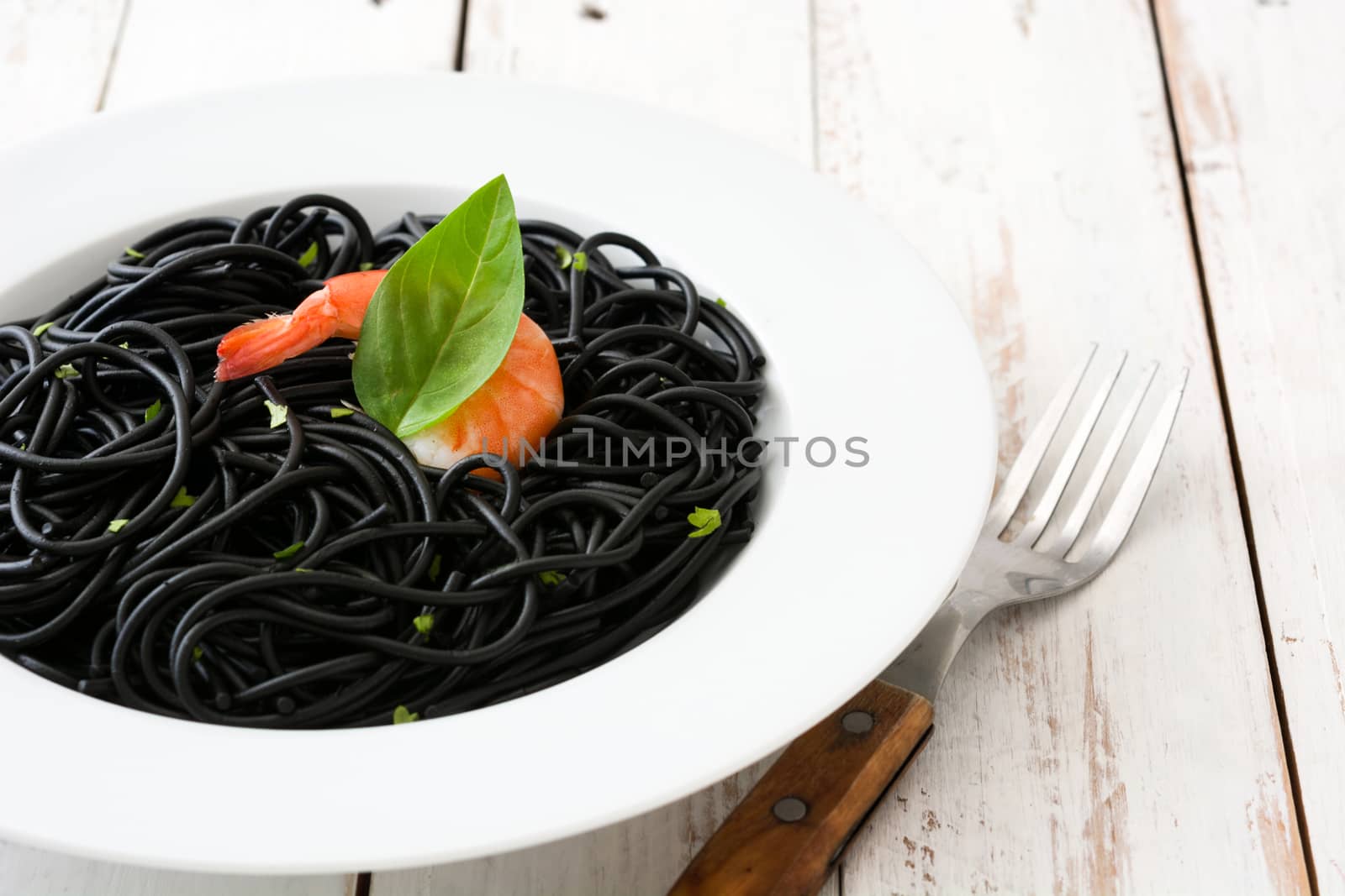 Black spaghetti with prawns on rustic wooden table by chandlervid85