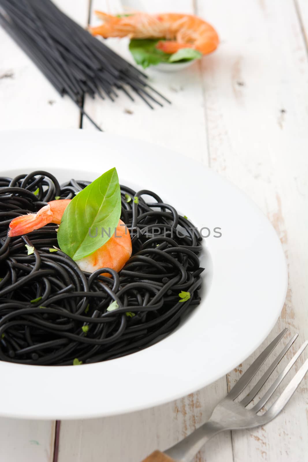 Black spaghetti with prawns on rustic wooden table by chandlervid85