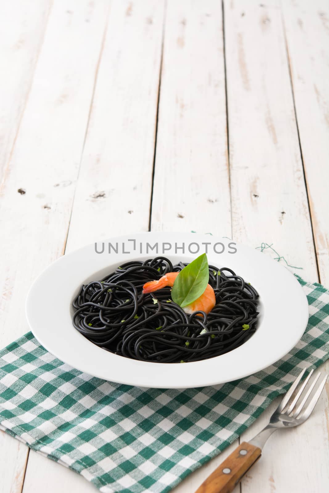 Black spaghetti with prawns on white wooden table