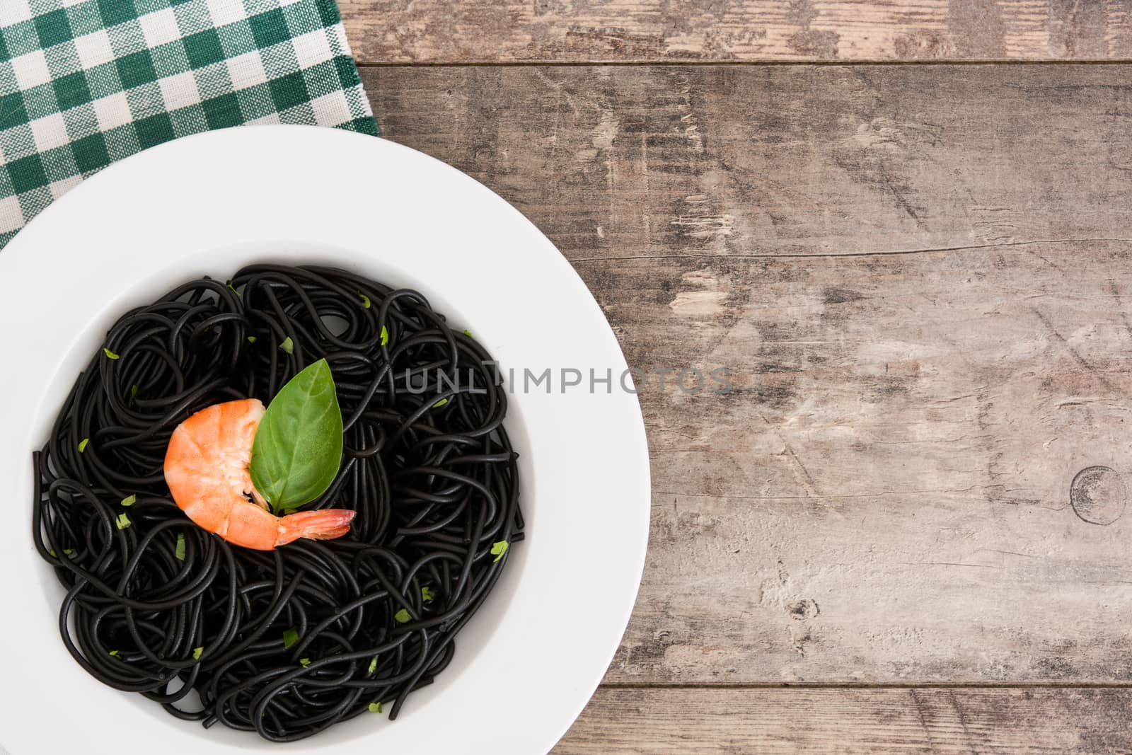 Black spaghetti with prawns and basil on wooden table by chandlervid85