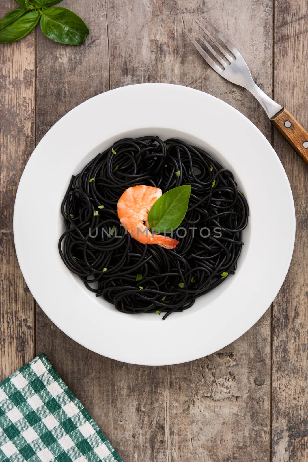 Black spaghetti with prawns on rustic wooden table by chandlervid85
