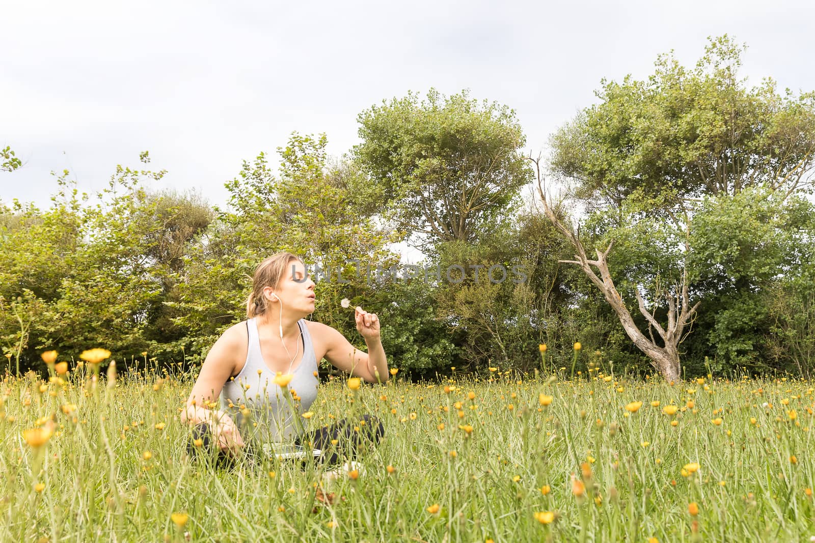 Woman in sportswear sitting in the park blowing a dandelion
