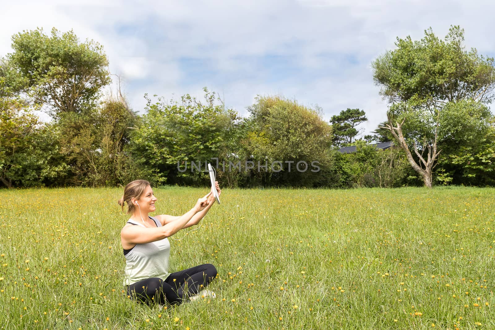 Woman in sportswear taking a self-portrait with a tablet sitting in the park