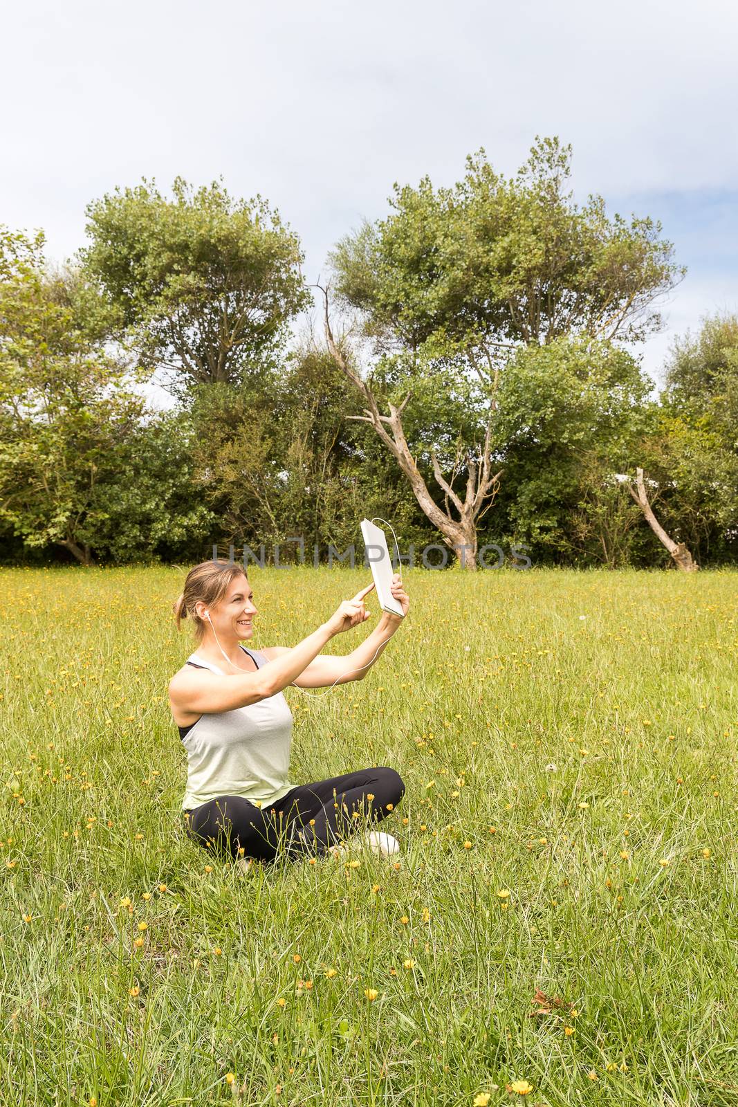 Woman in sportswear taking a self-portrait with a tablet sitting in the park