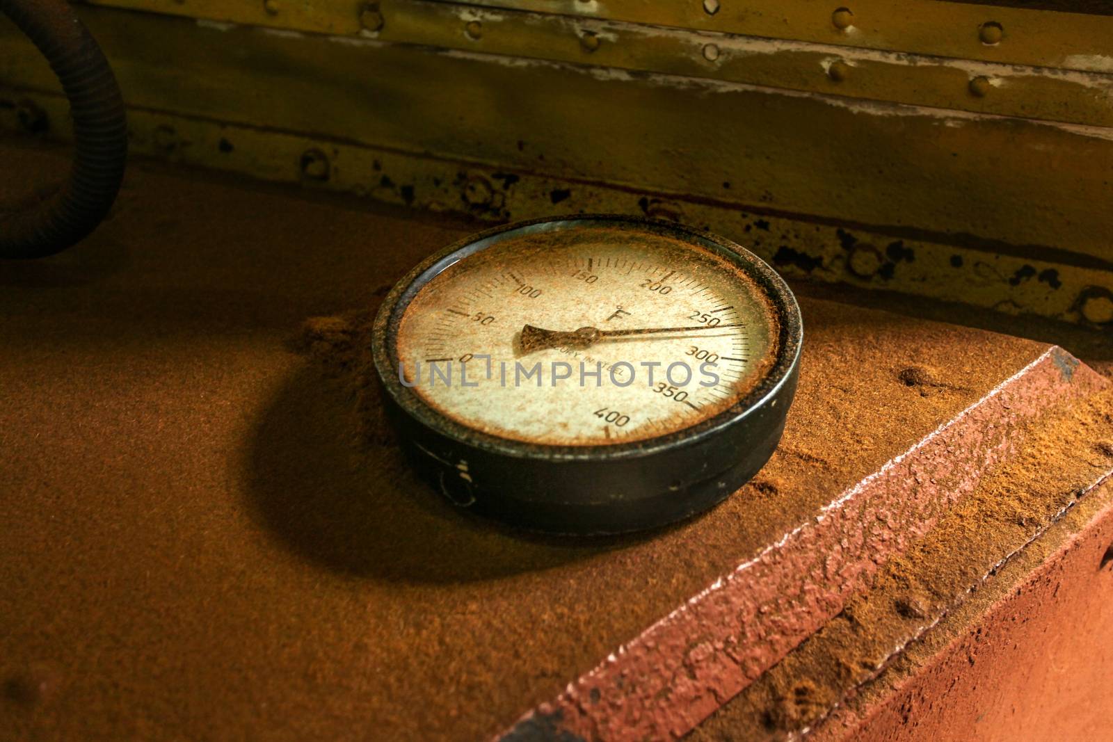 Old industrial circular thermometer gauge showing high temperature, on top of oven used to dry tea, covered with brown tea dust.