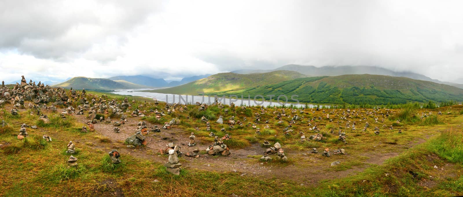 Small piles of stones made by tourists on viewpoint overlooking one of many scottish lochs in highlands.