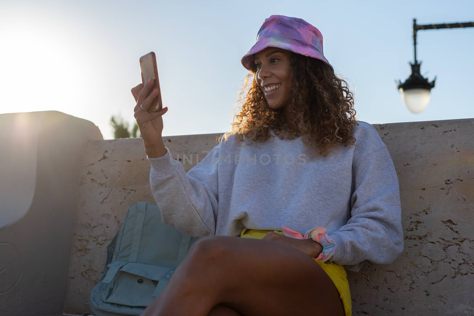 Portrait of an attractive young black woman sitting and talking with the mobile phone outdoors with her mask off. Concept communication