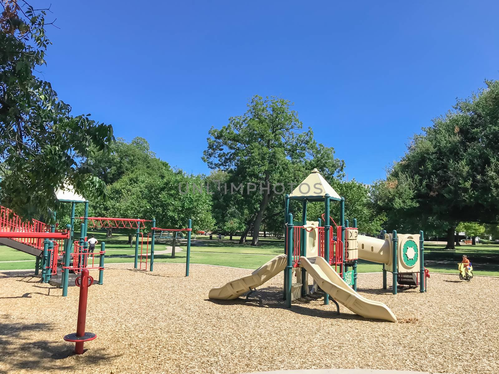 Unidentified toddler Asian boy playing in playground at public park surrounded by large trees in downtown Dallas, Texas, USA by trongnguyen