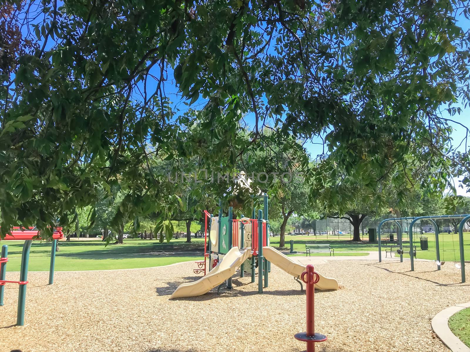 Shady from large trees and colorful urban playground at public park in downtown Dallas, Texas, USA by trongnguyen