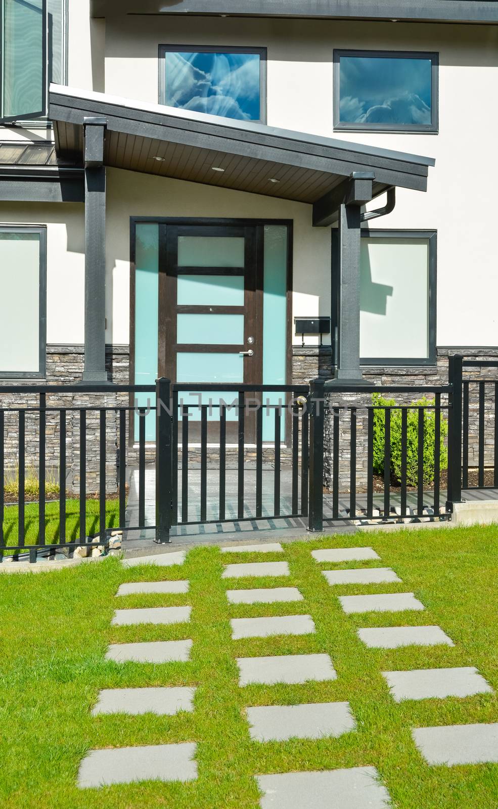 Entrance of new residential house with concrete tile pathway over front yard and metal fence in front