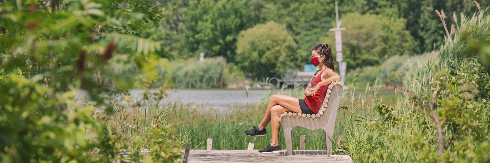 Mask wearing woman sitting relaxing on bench outside in summer nature park for coronavirus prevention. Protectve face covering COVID-19 lifestyle. Banner panoramic.