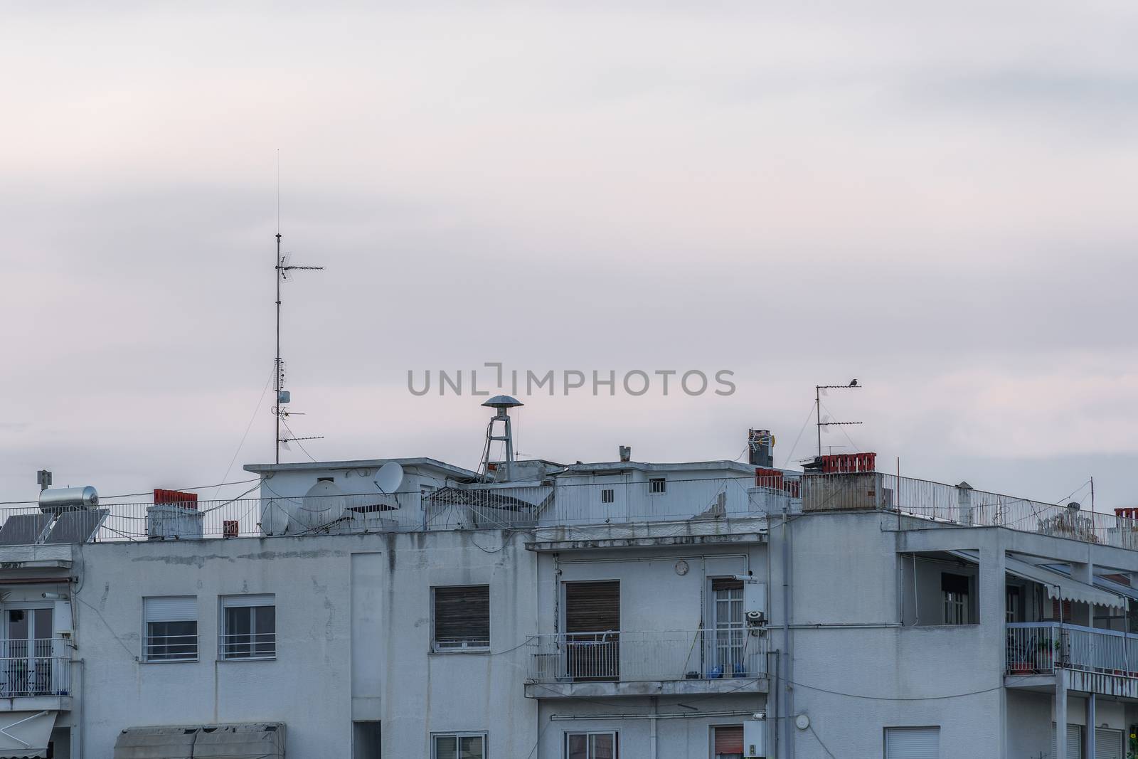Evening view of old mushroom shaped attack warning siren, between antennas and satellite dishes on top of city houses in Thessaloniki, Greece.