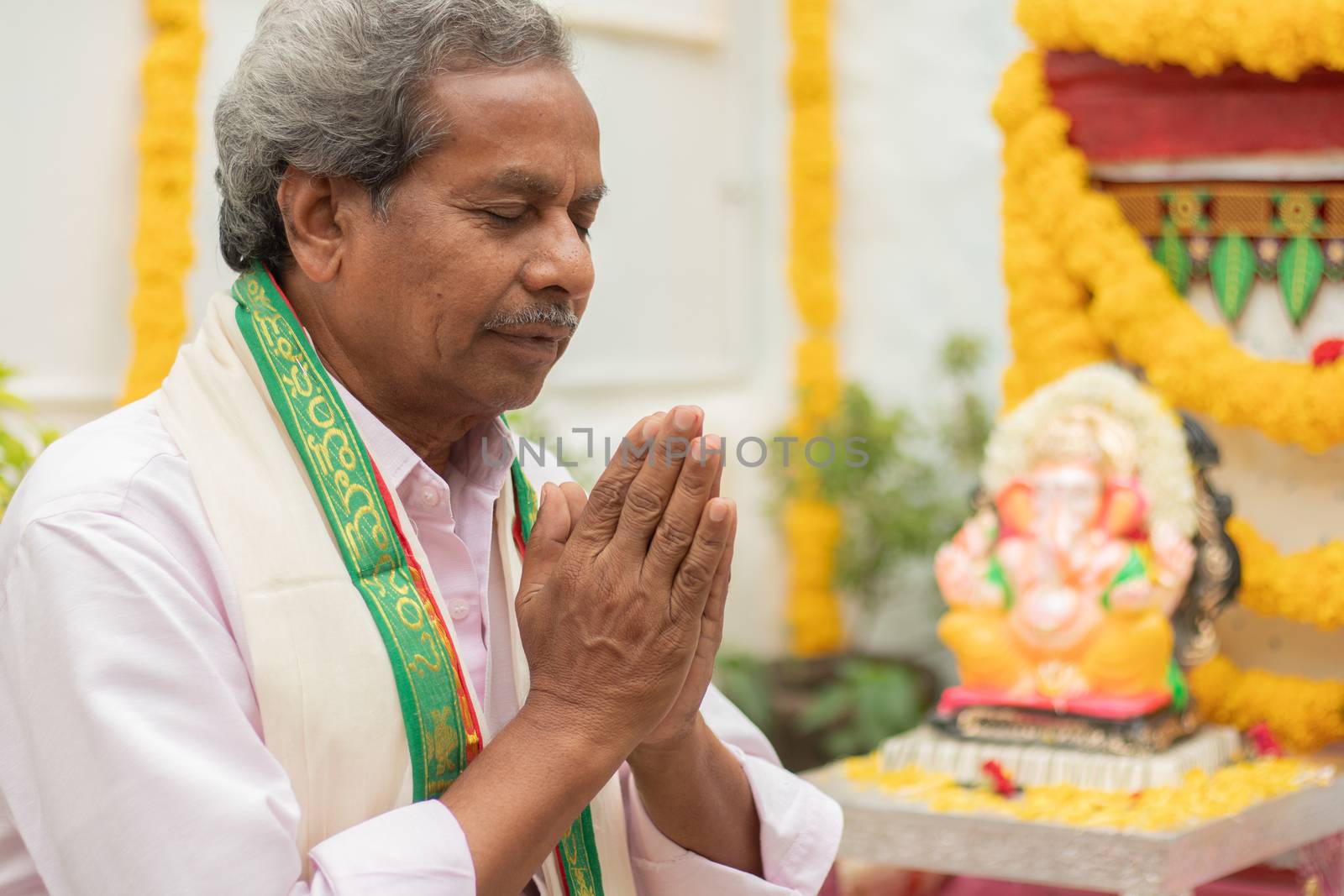 Elder man offering Prayer by namaste gesture in front of Lord Ganesha Idol during Ganesha or vinayaka Chaturthi festvial ceremony at home. by lakshmiprasad.maski@gmai.com