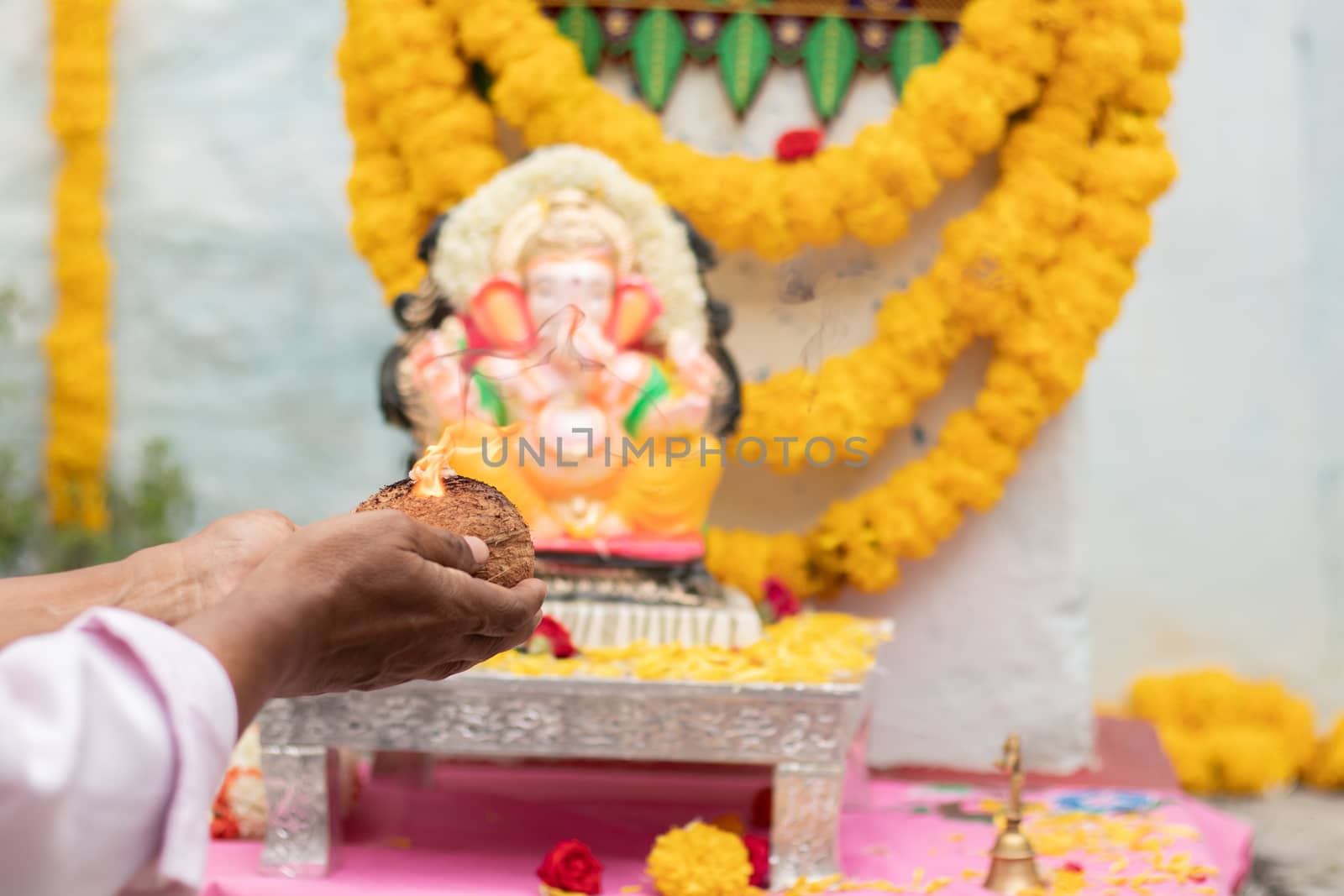 Closeup of Hands worshiping lord ganesh by offering aarti during vinayaka Chaturthi festival pooja or puja celebration at home in India.