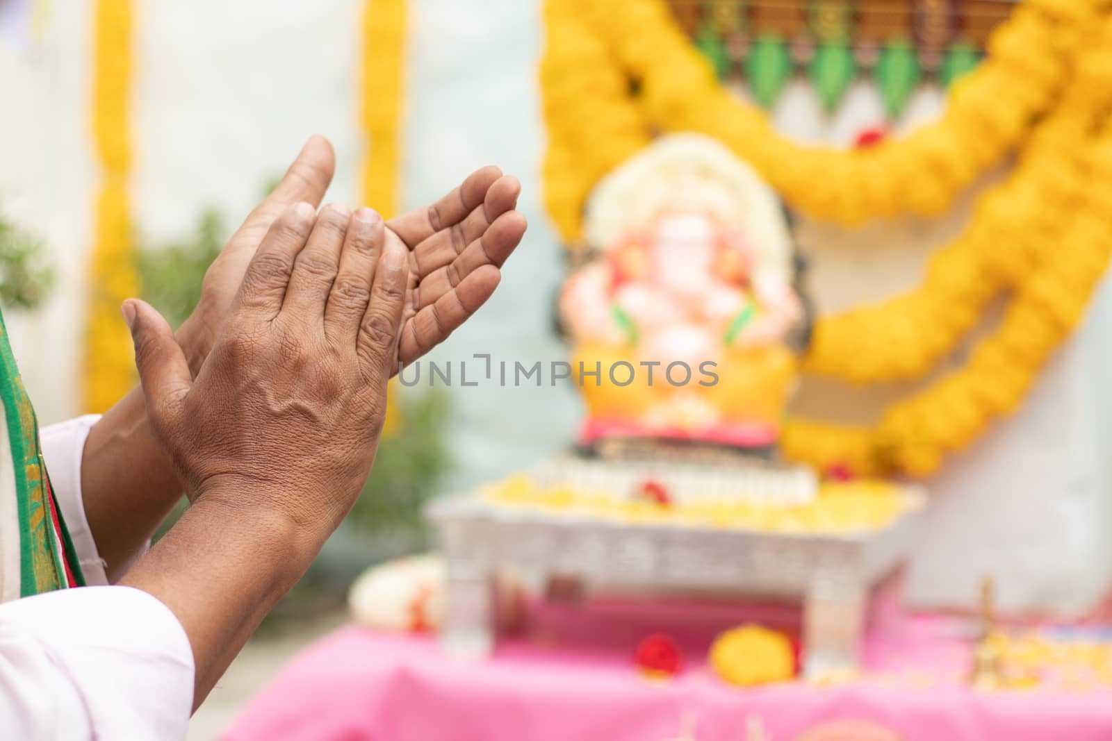 Close up of Elder man hands offering Bhajan or hymn in front of Lord Ganesha Idol by clapping during Ganesha or vinayaka Chaturthi festvial ceremony at home