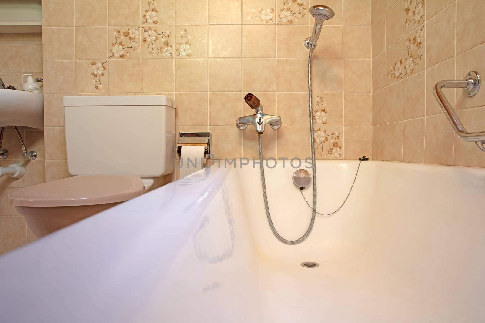Old bathroom, brown tiled interior with bathtub, assistive handle