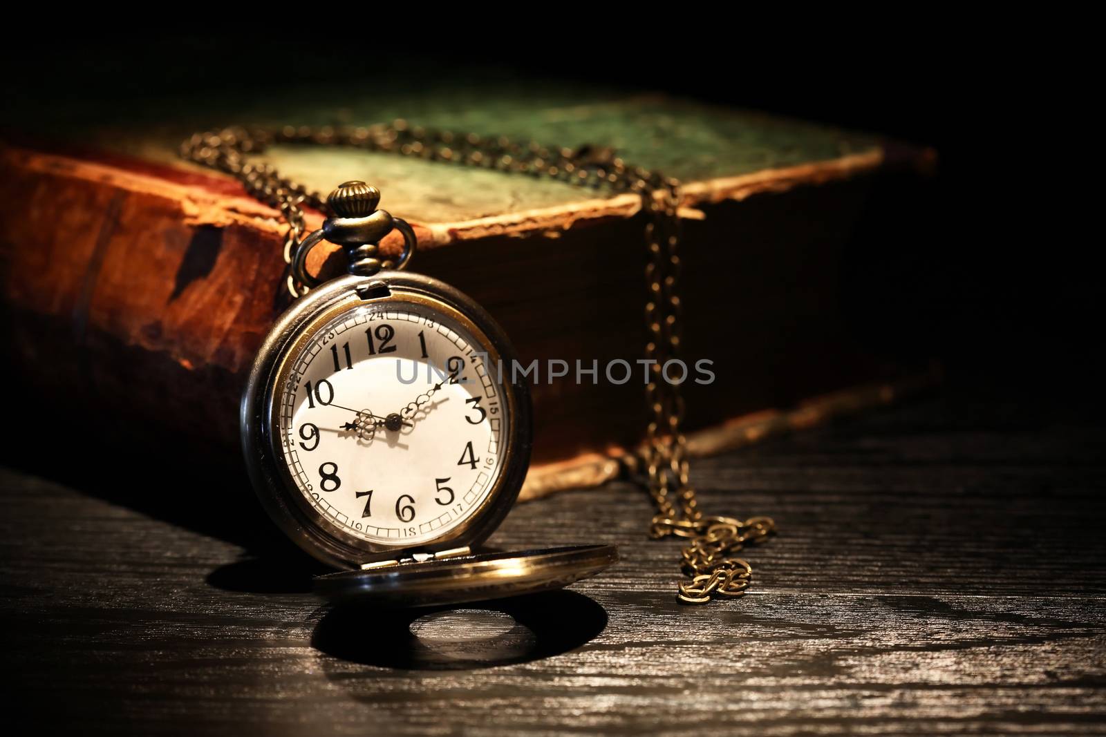 Old pocket watch near old book on dark background