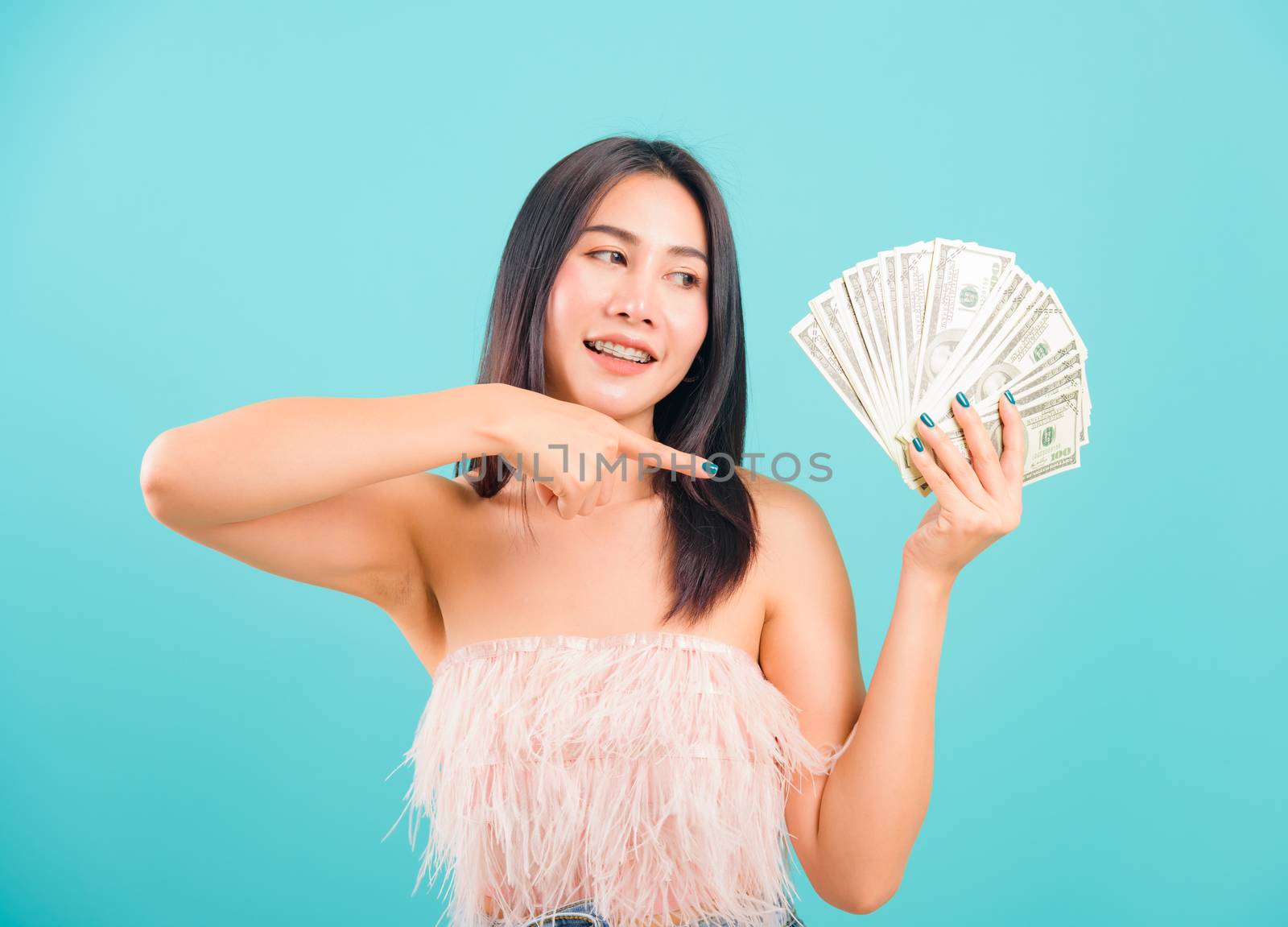 Smiling face portrait asian beautiful woman cheerful her holding and point the money on blue background, with copy space for text