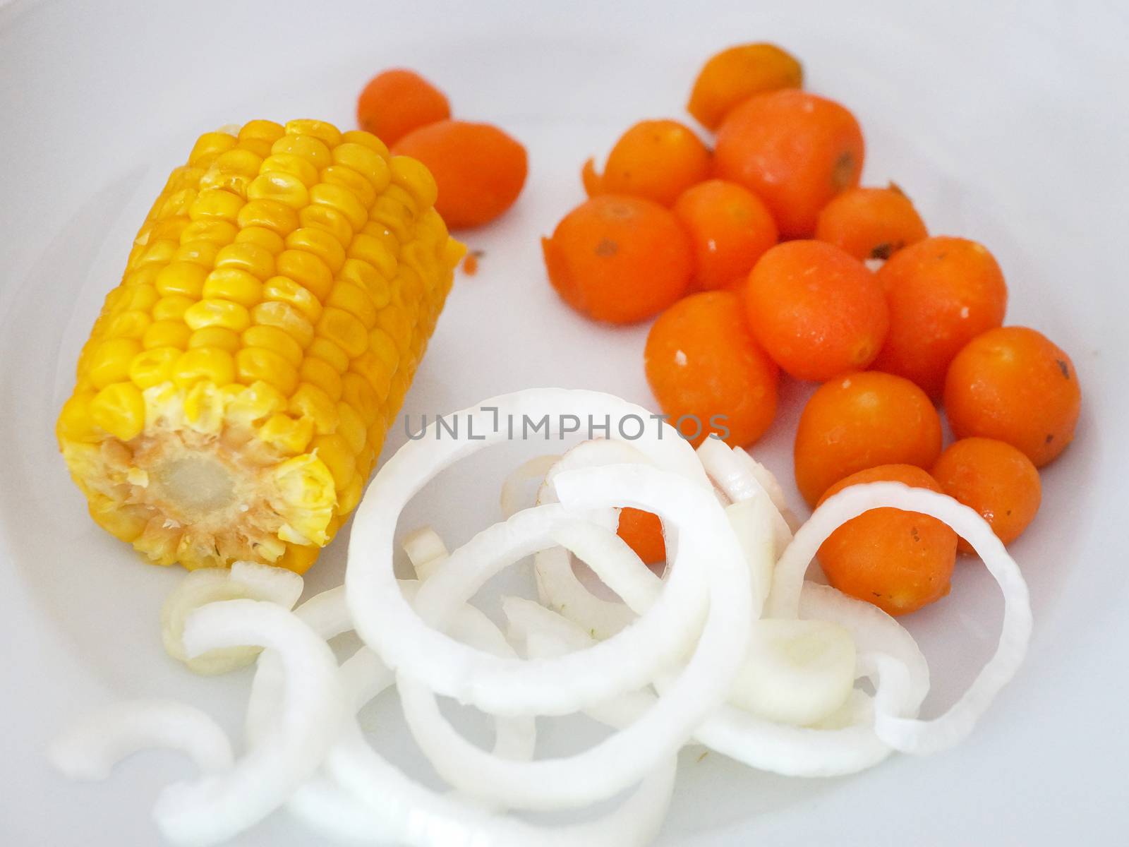 boiled vegetables - corn, carrots and onions in rings on a white plate by Annado