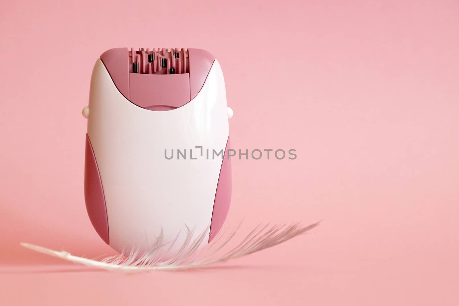 electric handheld epilator and feather on pink background close-up