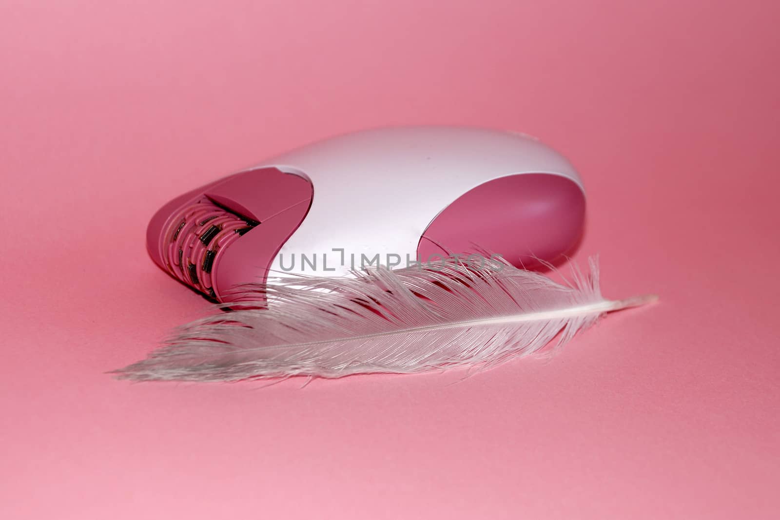 electric handheld epilator and feather on pink background close-up