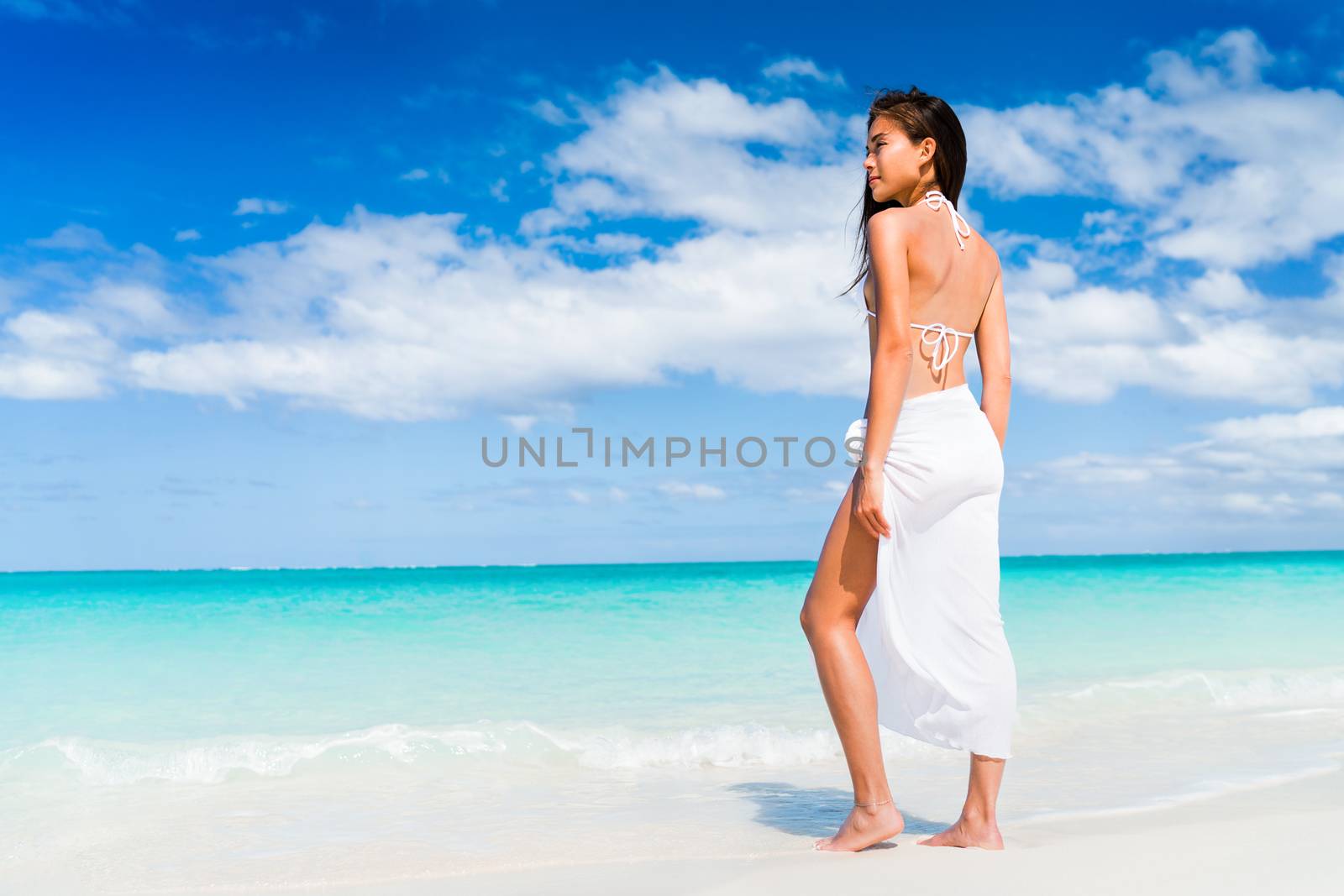 Elegant Asian woman in white beachwear bikini and fashion sarong standing on beach. Luxury travel vacation. Swimsuit swimwear model girl on summer holiday in the Caribbean by Maridav