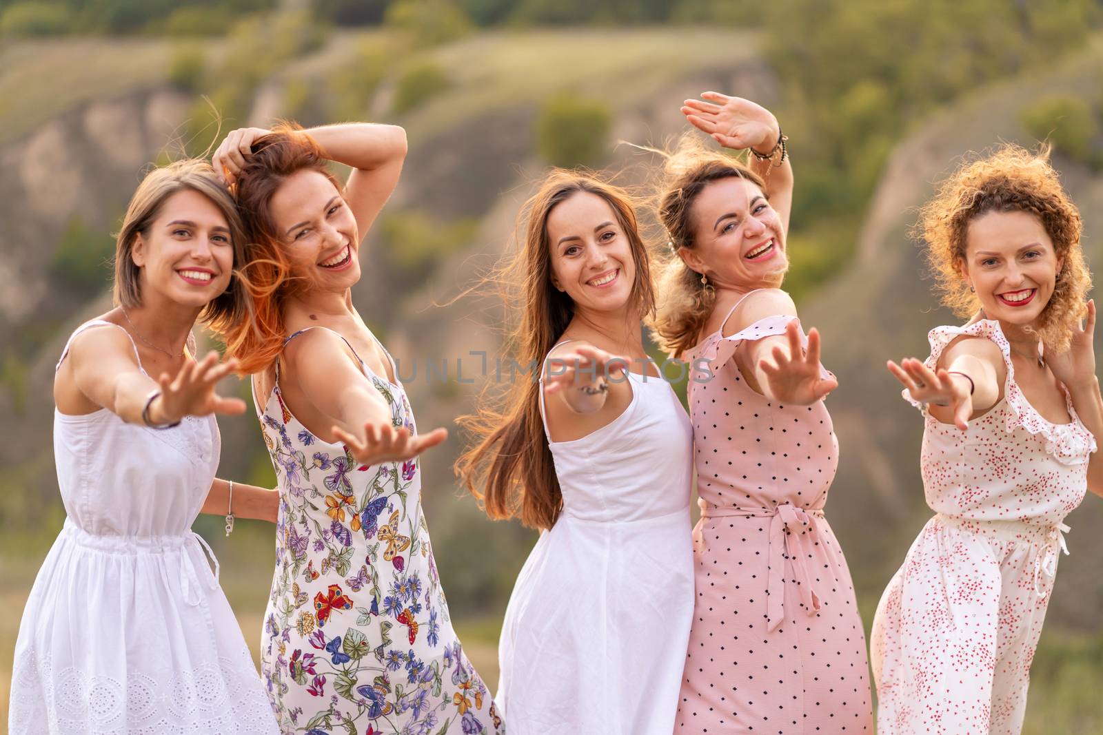 A cheerful company of beautiful girls friends enjoy the company and have fun together in a picturesque place of green hills