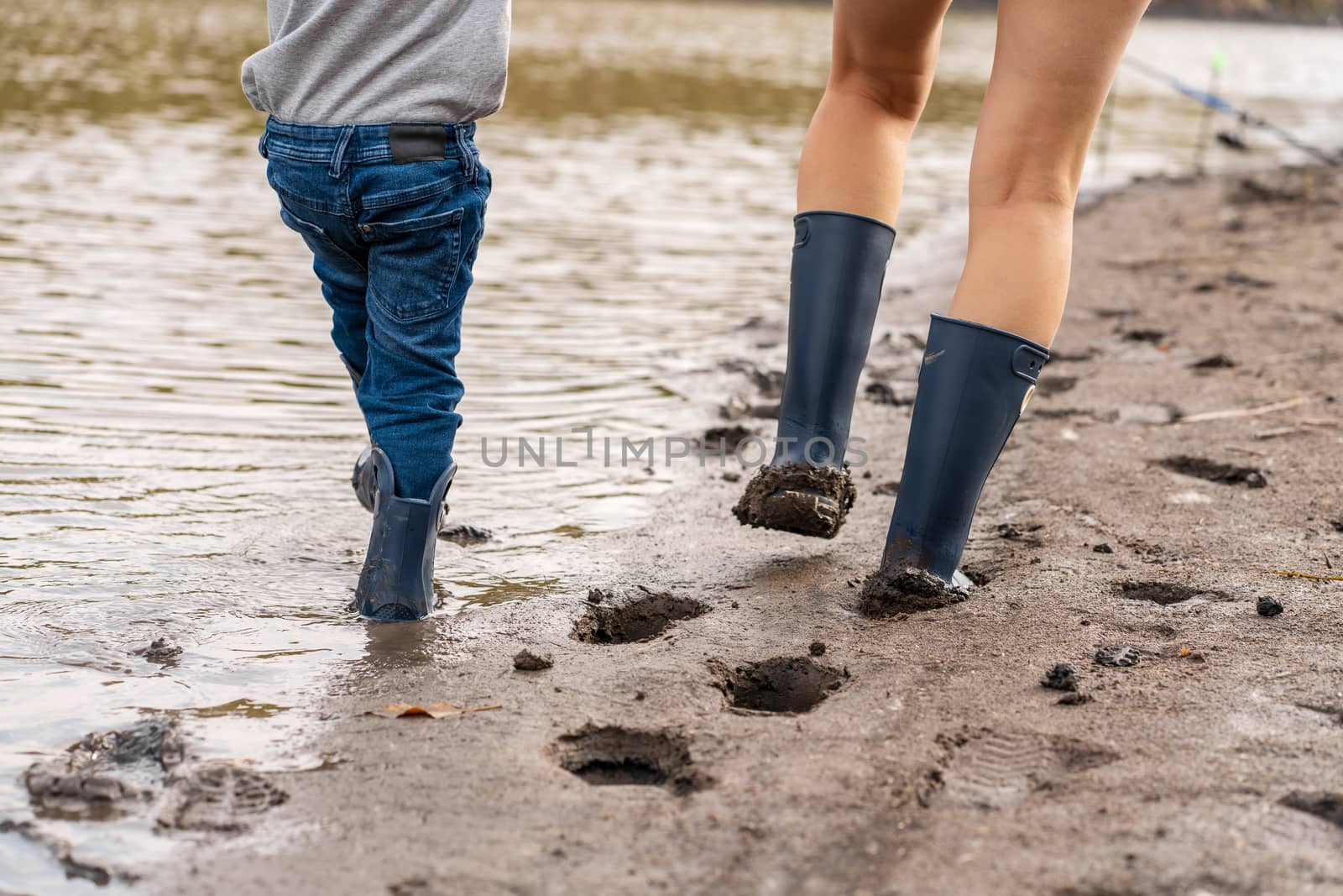 Mom with a small son walks along the sandy shore of the lake in rubber boots. Hanging out with children in nature, away from the city.