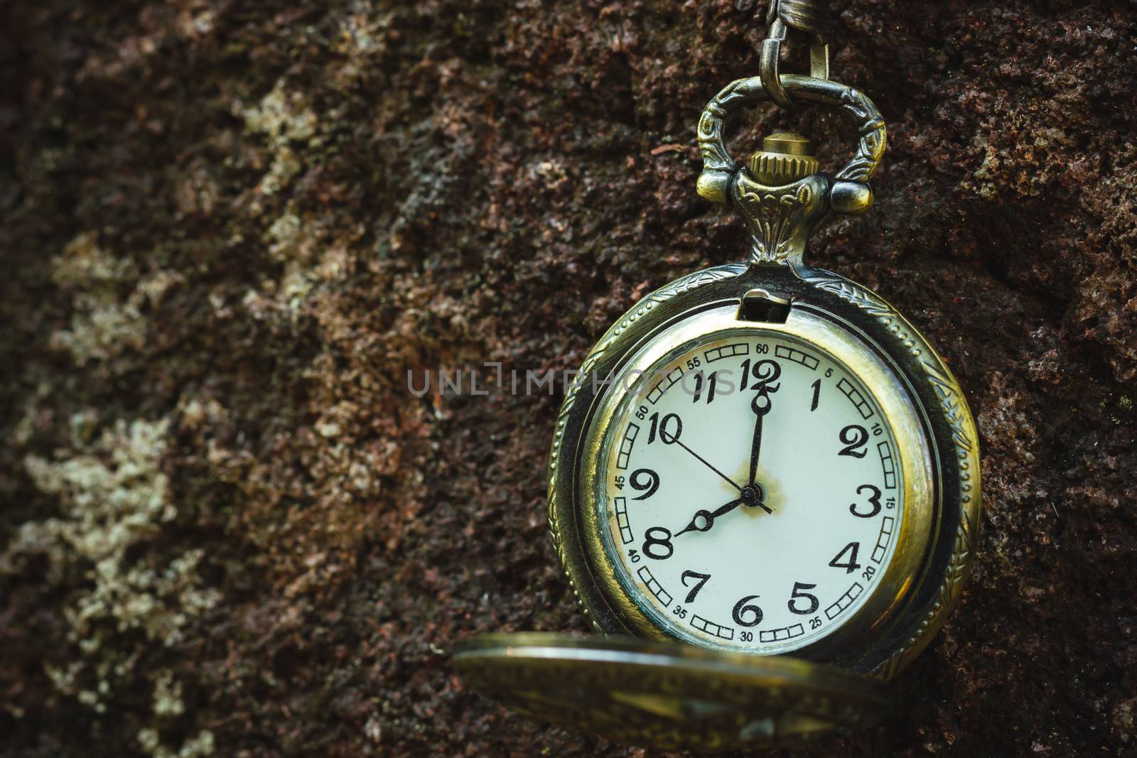 Vintage old pocket watch hanged on the rock background. by SaitanSainam