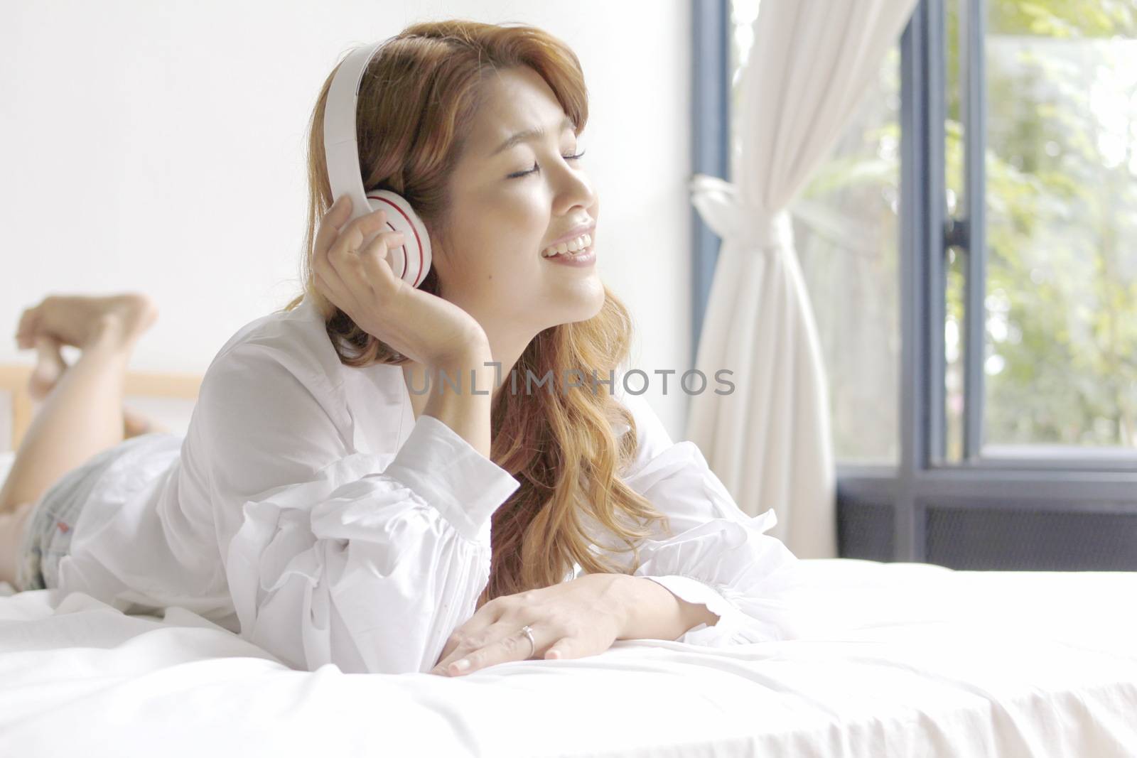 beautiful woman listening to music happily and lying in bed and smiling. Stay home concept by BirdKS