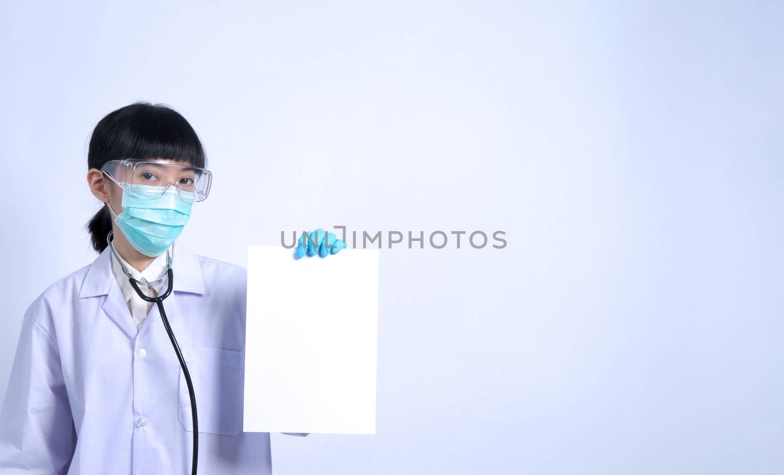 Asian woman doctor holding a blank paper in hand and copy space and she wear medical glove and face mask and doctor suit for protect virus pandemic. studio shot on plain background.