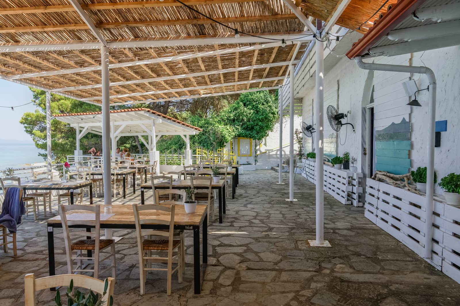 Restaurant outdoor seating area by the sea with a few customers in Kryopigi, Kassandra peninsula.