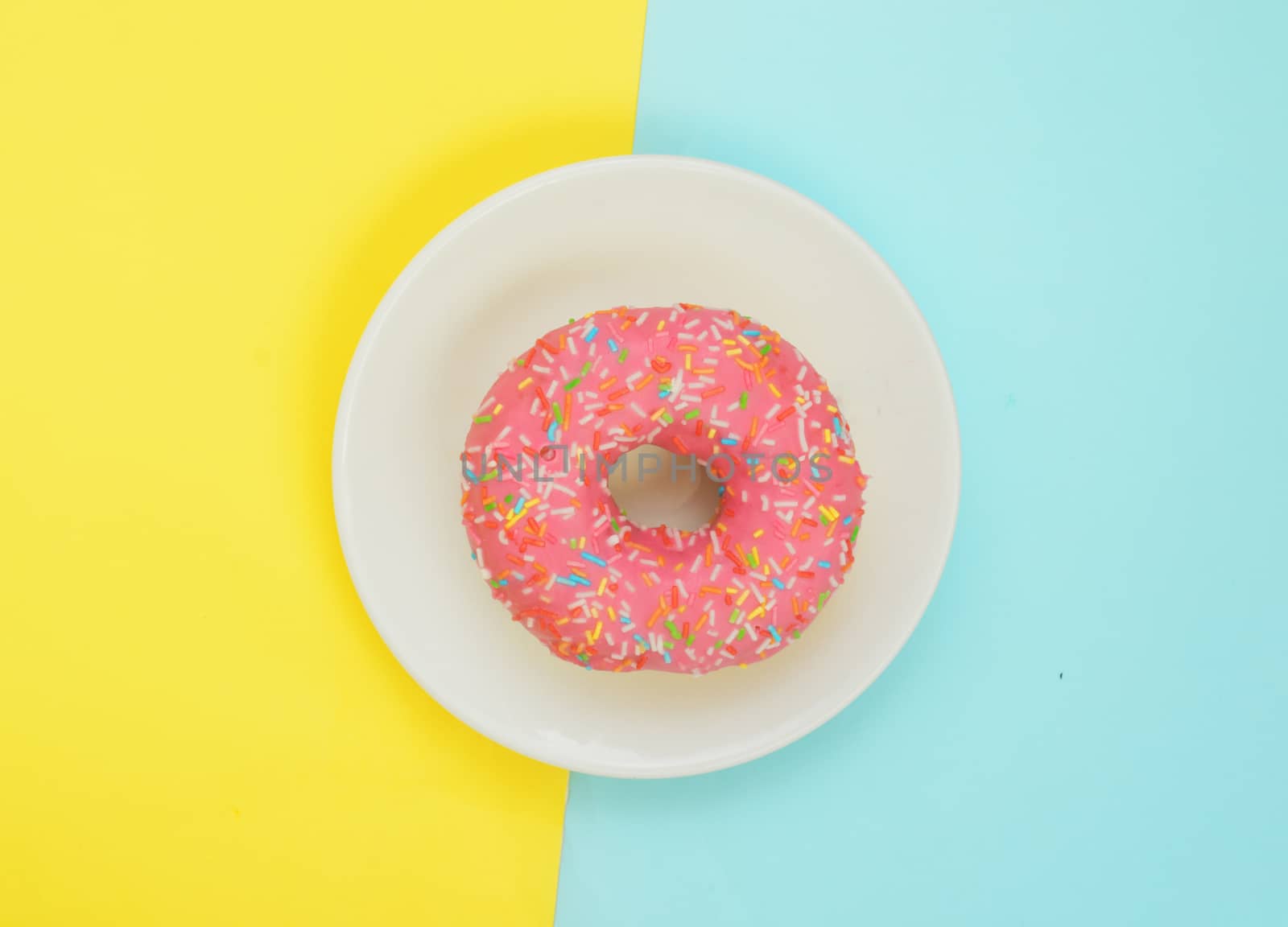 Top view,One pink glazed donut on white plate on pastel yellow turquoise background.Sweet dessert for snack.