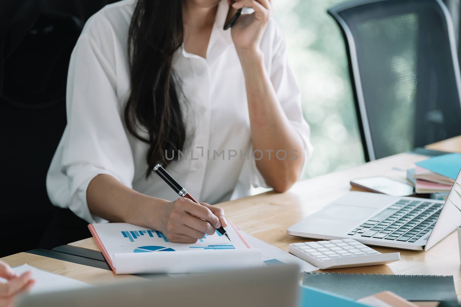 Young accountant hand holding smartphone to call marketing consultants and using laptop computer to analyze sales growth in the global workplace market. accounting concept.