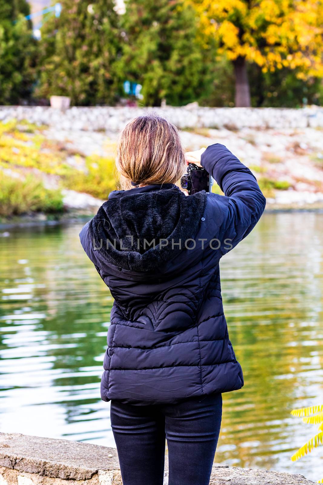 Girl taking photos of an autumn tree, autumn colors of a park in by vladispas