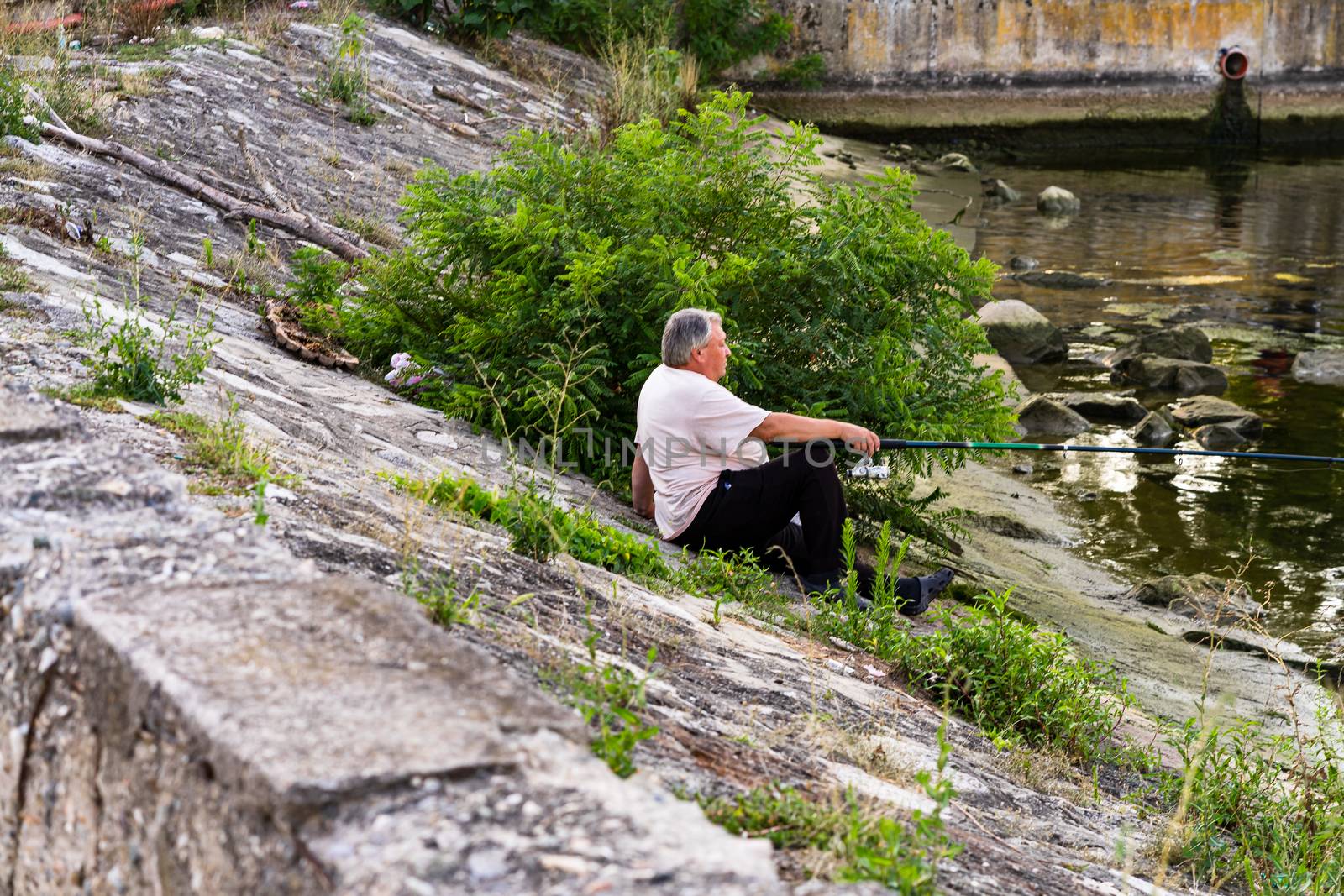 Man relaxing and fishing from the edge of a river in Orsova, Rom by vladispas