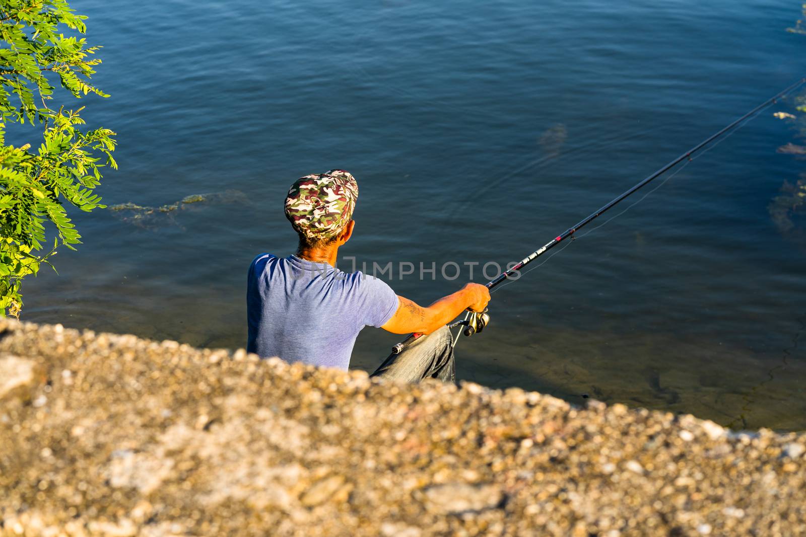 Man relaxing and fishing from the edge of a river in Orsova, Romania, 2020