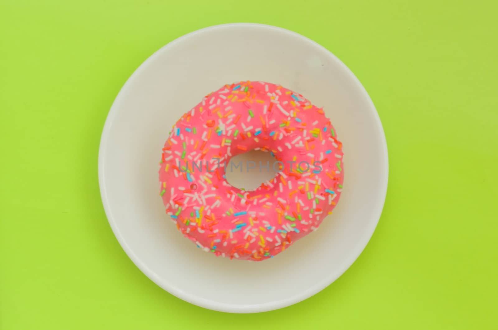 One pink glazed donut on white plate on green background, sweet dessert for snack.