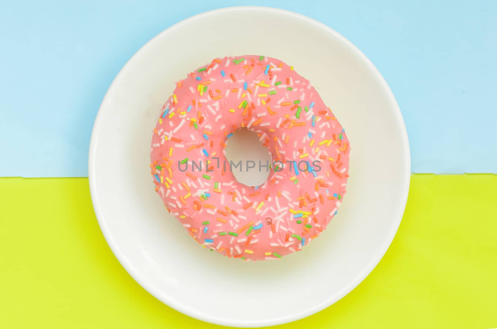 Top view, pink glazed donut on white plate on pastel green turquoise background.Sweet dessert for snack.